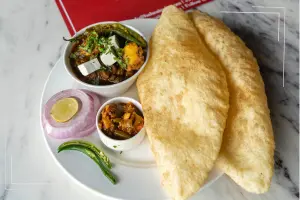 Delicious plate of fluffy bhature with paneer sabzi, green chili, onions, and pickles served on a white plate.