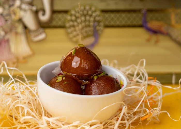 a white bowl filled with three syrup-soaked gulab jamun, garnished with nuts