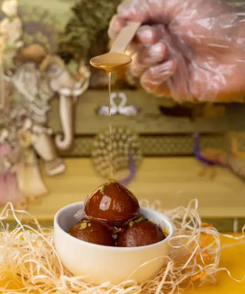 a white bowl filled with three syrup-soaked gulab jamun, garnished with nuts