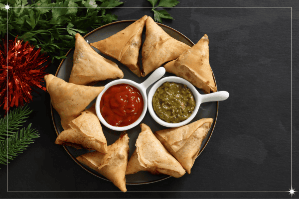 A plate is full of samosas, green and red chutney bowl chutney